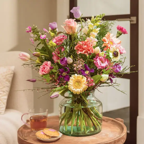 Pastelkleurig plukboeket met rozen, gerbera en seizoensbloemen in glazen vaas op ronde tafel