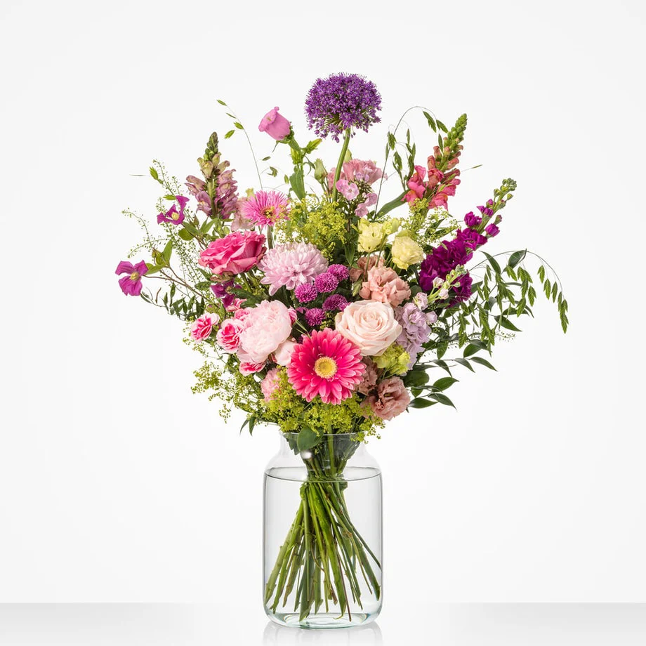 Boeket met rozen, gerbera, pioenroos, allium en leeuwenbek in een glazen vaas