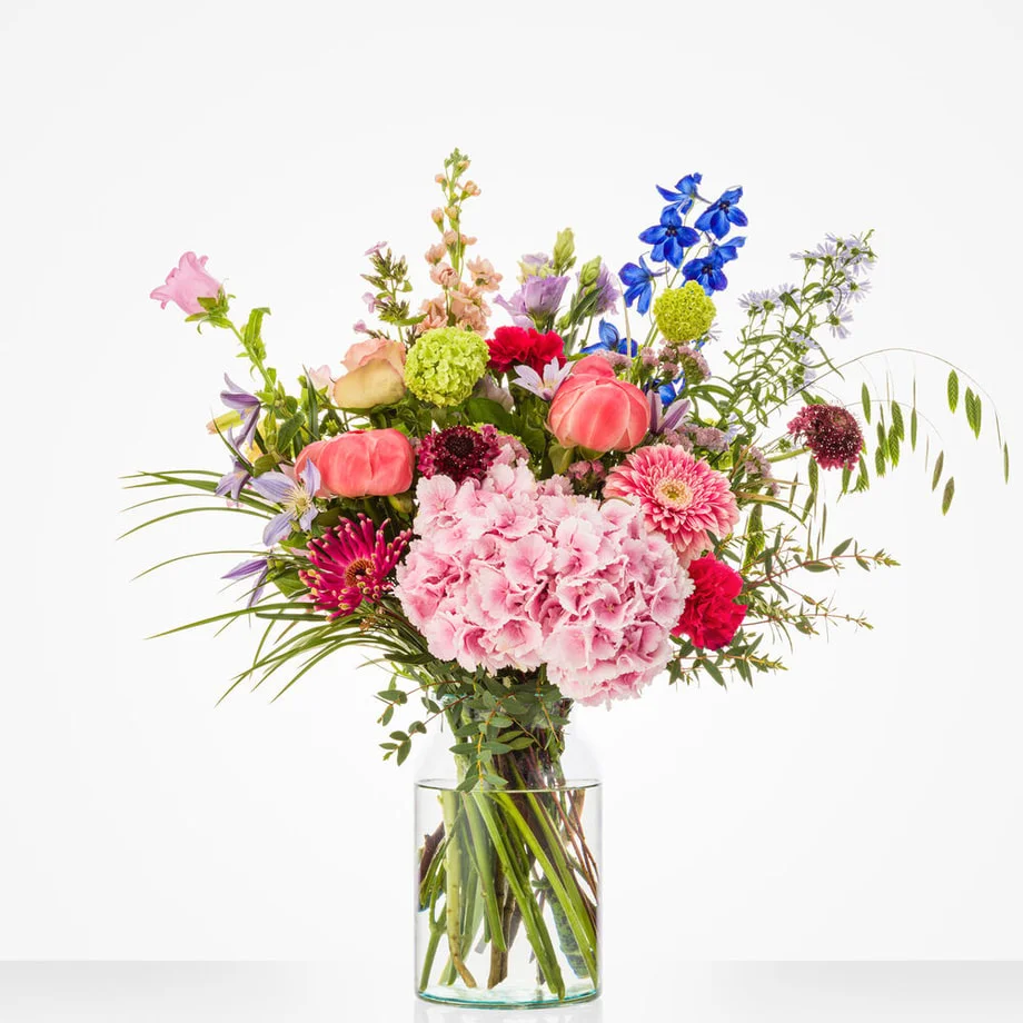 Boeket met roze hortensia, gerbera, rozen en blauwe delphinium in een glazen vaas