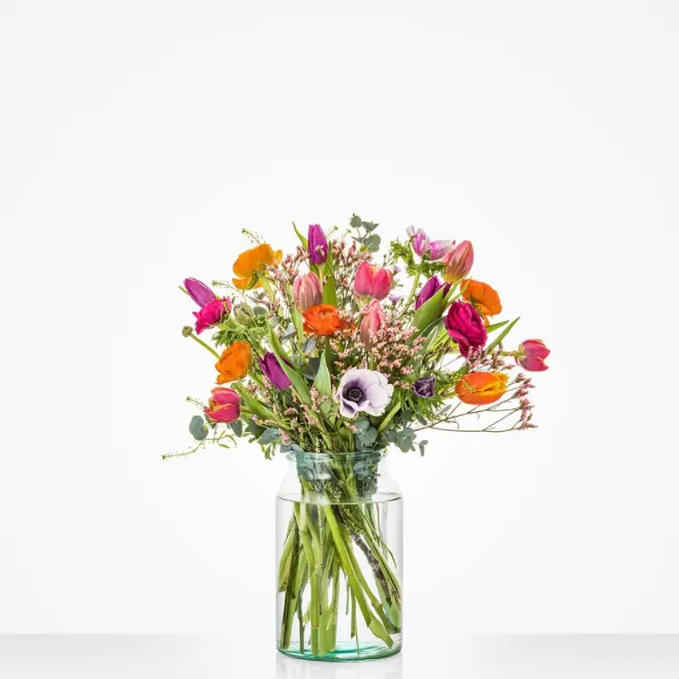 Veldboeket met tulpen, anemonen en oranje bloemen in glazen vaas