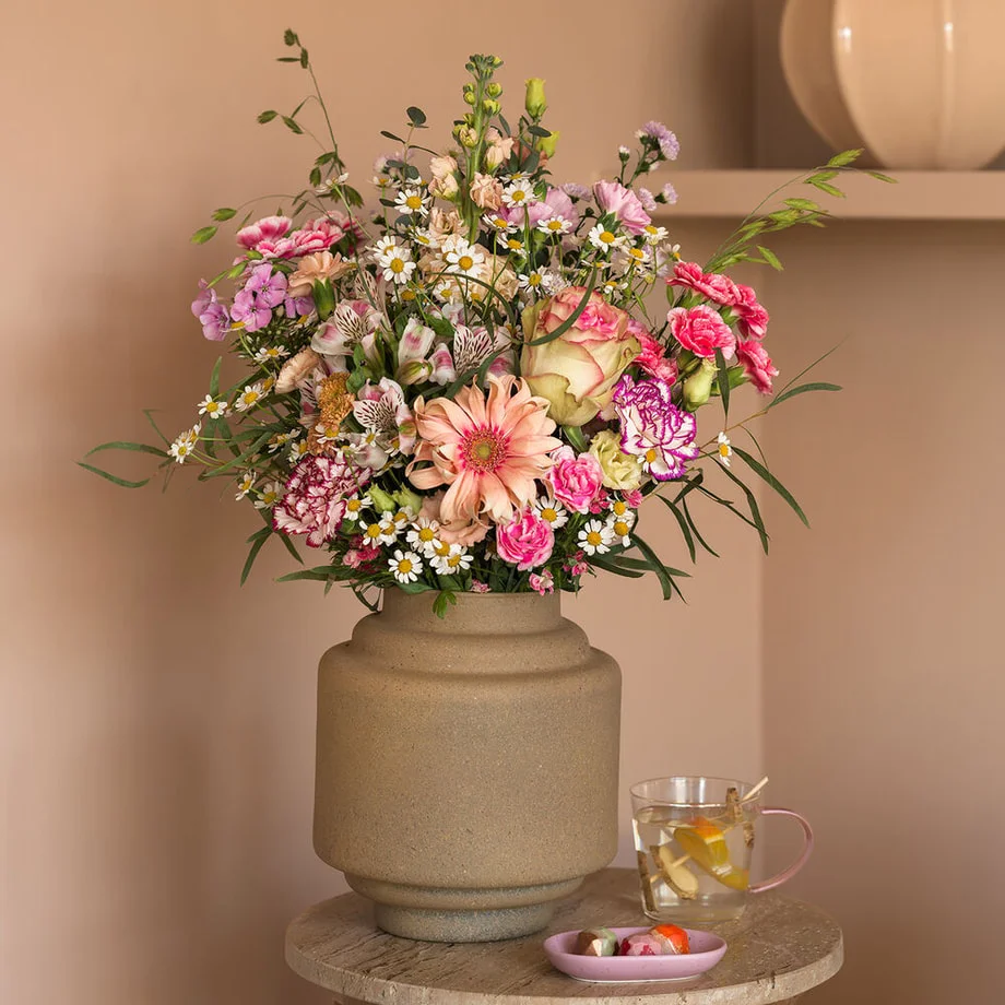 Boeket met gerbera, rozen, anjers, kamille en alstroemeria in een keramieken vaas in huiselijke setting