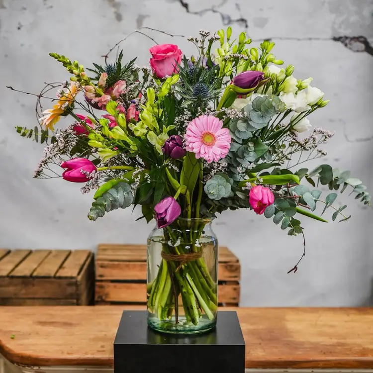 Veldachtig boeket met tulpen, rozen en eucalyptus in glazen vaas op pilaar