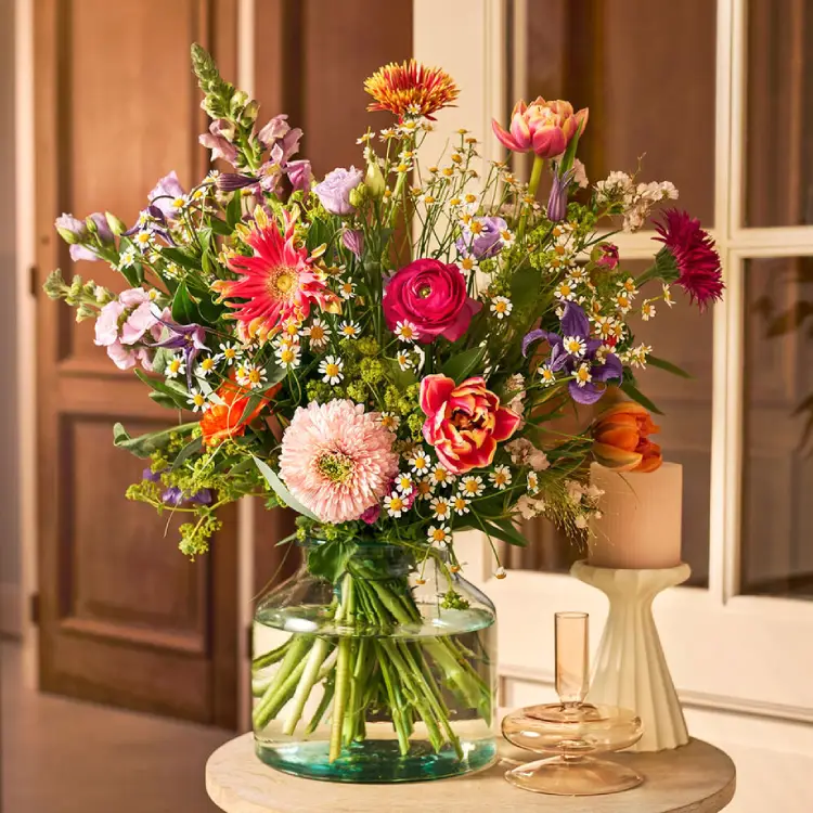 Vrolijk plukboeket met tulpen, gerbera en kamille in glazen vaas op tafel