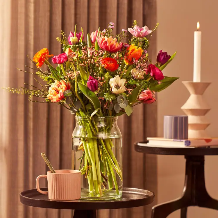 Veldboeket met tulpen, anemonen en oranje bloemen in glazen vaas op tafel