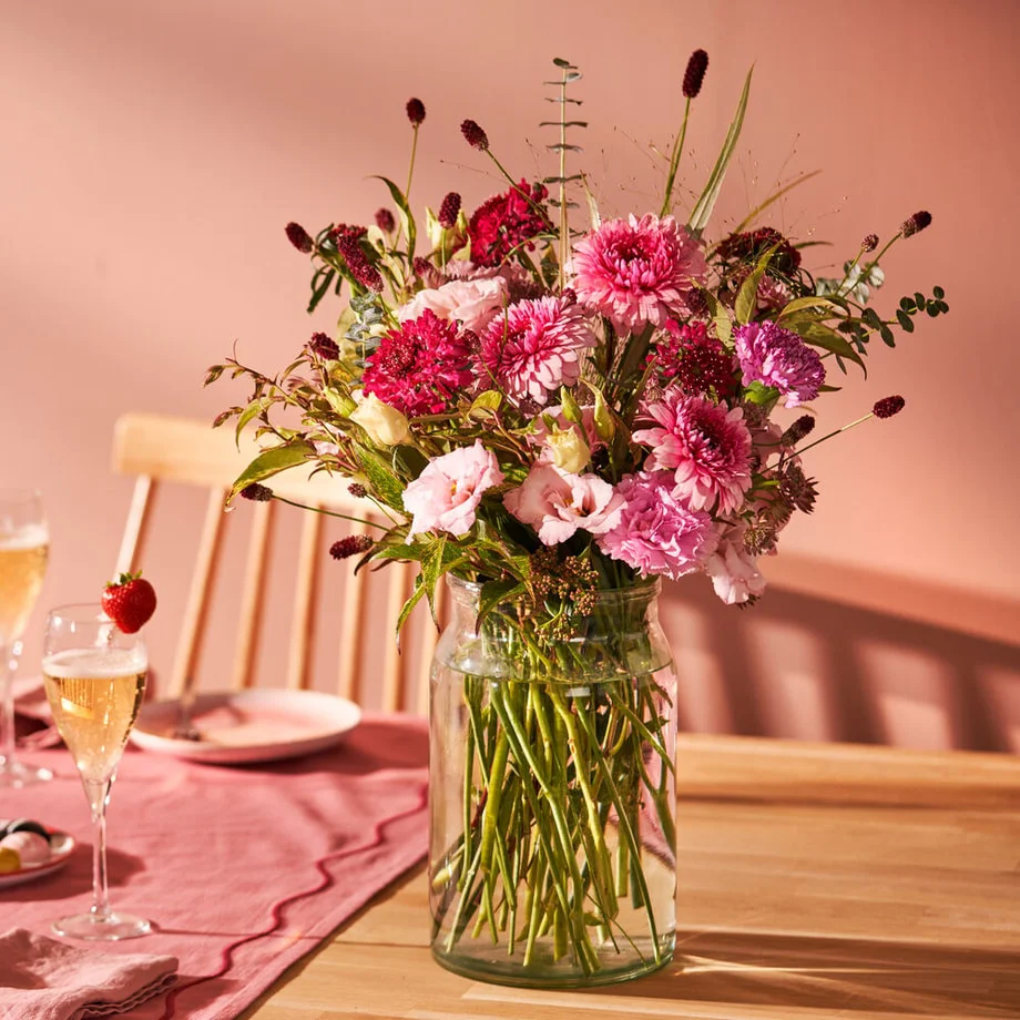 Boeket met roze chrysanten, lisianthus en rode accenten in een glazen vaas op houten tafel