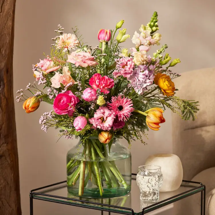 Voorjaarsboeket met gerbera, anjers en oranje accenten in glazen vaas op tafel