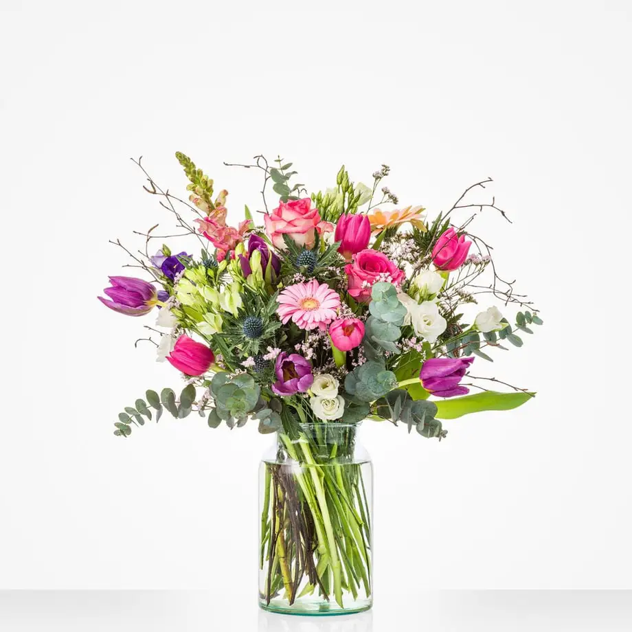 Veldachtig boeket met tulpen, rozen en eucalyptus in glazen vaas