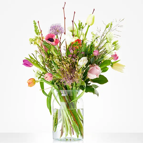 Luchtig plukboeket met tulpen, anemonen en voorjaarsgroen in glazen vaas