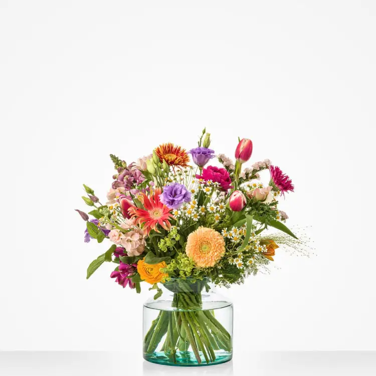 Vrolijk plukboeket met tulpen, gerbera en kamille in glazen vaas